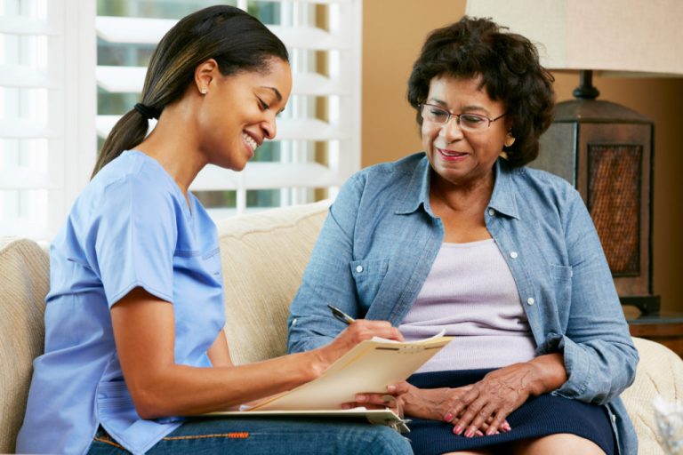 A professional female home safety consultant sitting on a living room couch next to a client, warmly discussing home optimization and fall prevention services.
