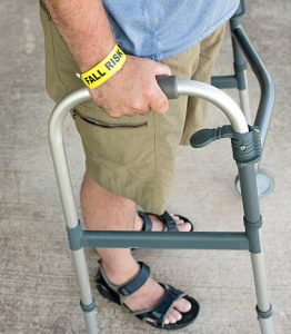 Older adult man using a walker with a fall risk wrist brace, representing mobility challenges and the need for home safety and fall prevention