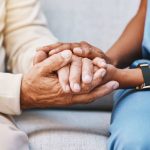 Close-up of a compassionate home safety consultant gently holding the hands of an older adult, symbolizing support, fall prevention, and trust in a home setting.
