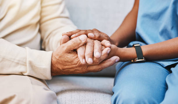 Close-up of a compassionate home safety consultant gently holding the hands of an older adult, symbolizing support, fall prevention, and trust in a home setting.