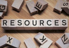 Wooden toy letter blocks arranged in a line to spell out the word RESOURCES on a light wooden background, surrounded by other scattered letter blocks.
